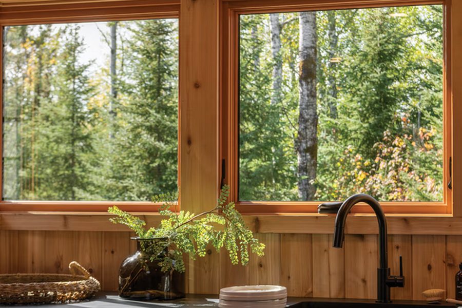 Two Marvin Ultimate Awning windows in a cedar-lined kitchen above a sink, looking into woodland